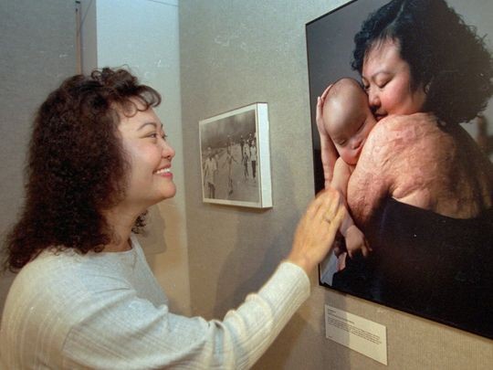 Bà Phúc đang ngắm tấm ảnh bà ôm con trai đầu lòng. Bên cạnh là bức hình nổi tiếng "Em bé Napalm". Ảnh: Nick Út/AP.