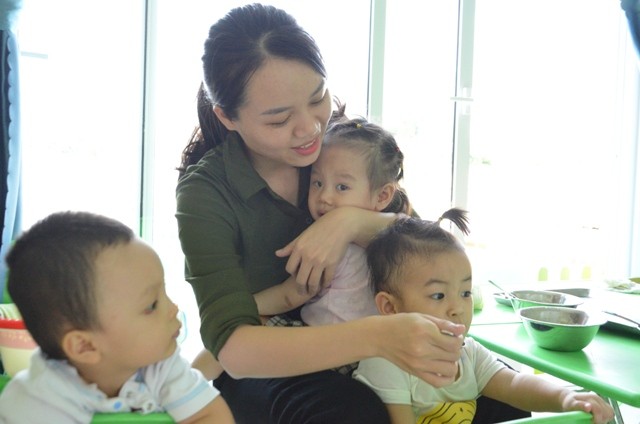 Giờ ăn của nhóm trẻ 6 - 12 tháng tuổi tại Trường Mầm non Hoàng Cúc (Q. Sơn Trà, TP Đà Nẵng), GV vừa phải bồng trẻ vỗ về vừa cho các bé khác ăn. 