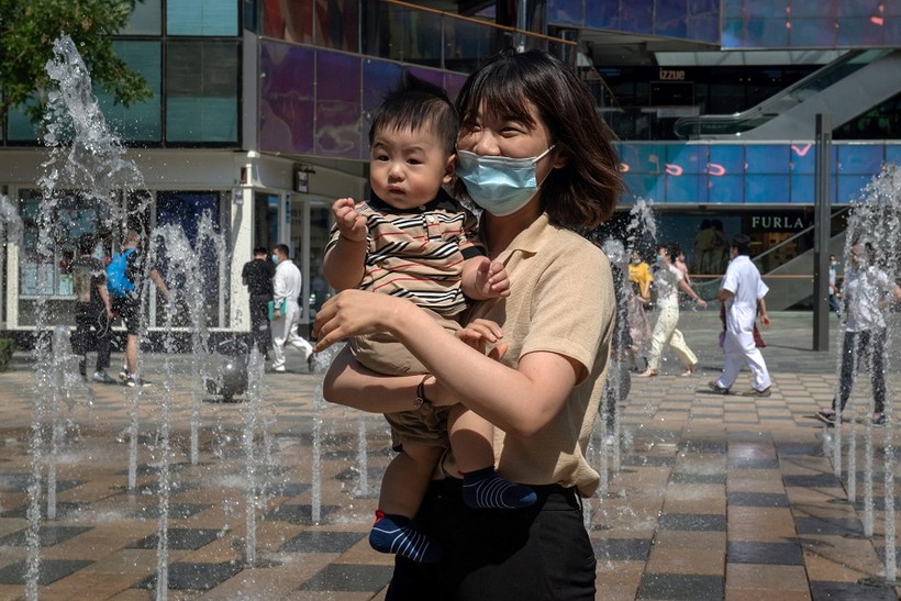Một người phụ nữ bế con bên ngoài trung tâm mua sắm ở Bắc Kinh, Trung Quốc. (Ảnh: Nicolas Asfouri/AFP).
