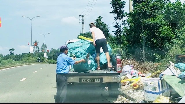 Hai người đàn ông dùng xe bán tải chở rác vứt ra đường quốc lộ.
