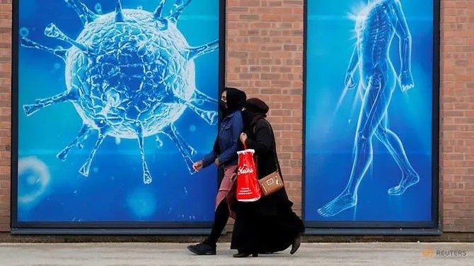 Người dân đi qua hình ảnh minh họa virus bên ngoài trung tâm khoa học khu vực ở Oldham, Vương quốc Anh, giữa đại dịch COVID-19.