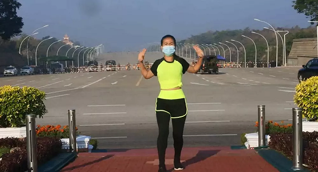 Người phụ nữ tập aerobics khi xe quân sự chạy sau lưng.