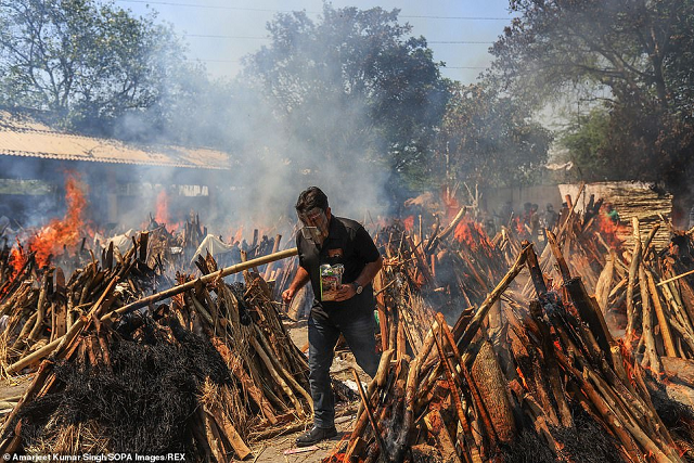 Một người đàn ông thực hiện các nghi lễ cuối cùng cho người thân của mình trong khi giàn thiêu của những người đã khuất Covid-19 rực lửa tại một điểm hỏa táng ở New Delhi.