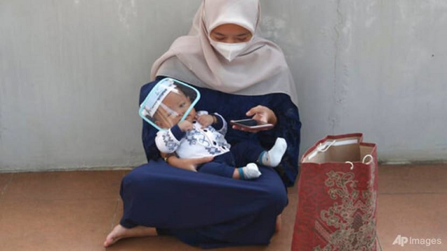 Một phụ nữ Indonesia đang bế em bé đeo tấm chắn phòng dịch.