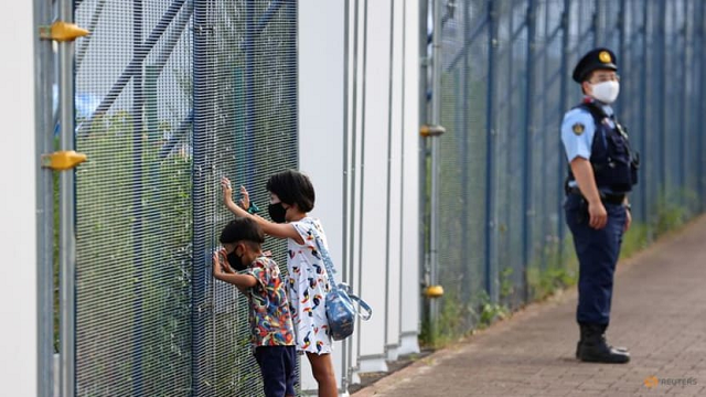 2 em nhỏ Nhật Bản đeo khẩu trang nhìn qua hàng rào của Công viên Thể thao Đô thị Aomi.
