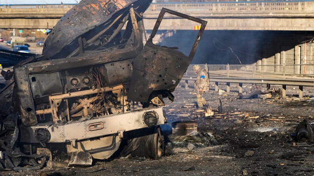 Một người lính Ukraine đi ngang qua một chiếc xe tải quân sự bị cháy trên đường phố ở Kiev, Ukraine, hôm thứ Bảy