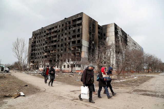 Mọi người đi bộ gần một tòa nhà bị phá hủy trong cuộc tấn công của Nga ở thành phố cảng Mariupol.