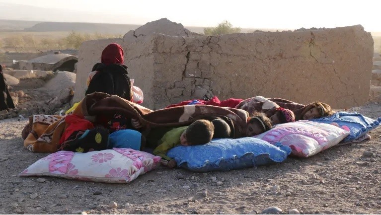 Trẻ em Afghanistan nằm ngủ bên cạnh những ngôi nhà bị hư hại sau trận động đất ở làng Sarbuland, Zendeh Jan, ngày 7/10.