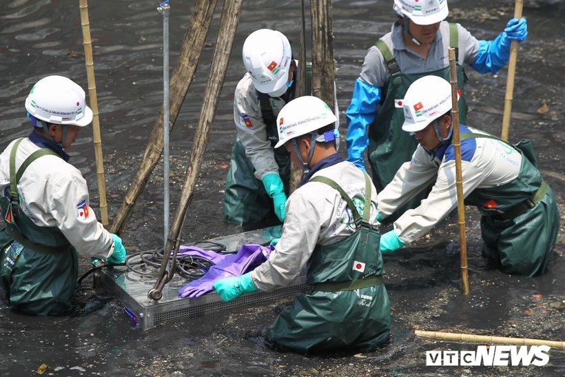 Các công nhân kỹ thuật đưa thiết bị làm sạch xuống lòng sông Tô Lịch tại Lễ khởi động ngày 16/5.