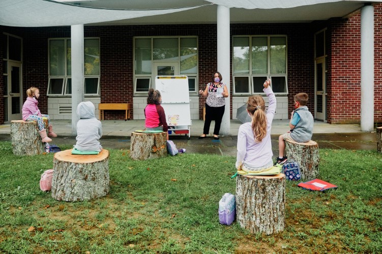 Trẻ em tại Trường Falmouth ngồi trên gốc cây để học.