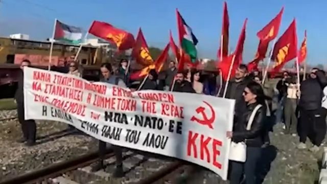Các đảng viên KKE và tổ chức thanh niên KNE giơ cao cờ và biểu ngữ để chặn đoàn tàu chở xe tăng Abrams của Mỹ đang trên đường tới Bulgaria