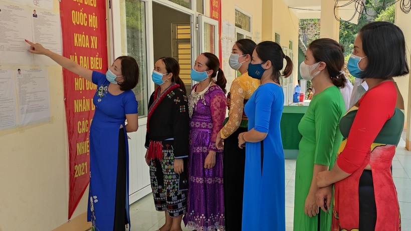 Bà Ngô Thị Lan - Hiệu trưởng Trường Tiểu học Pù Nhi, huyện Mường Lát, tỉnh Thanh Hóa (áo dài màu xanh đậm) đang cùng giáo viên nhà trường tìm hiểu danh sách các ứng cử viên tại điểm bầu cử.