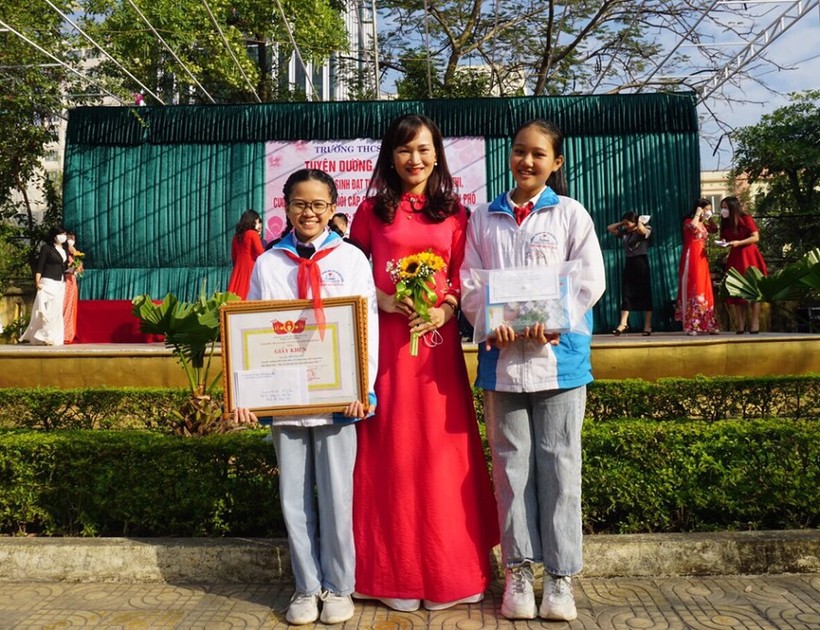 Đỗ Vy Lam (bìa trái) cùng cô giáo chủ nhiệm Cao Thị Hằng trong buổi lễ tuyên dương của Trường THCS Điện Biên.