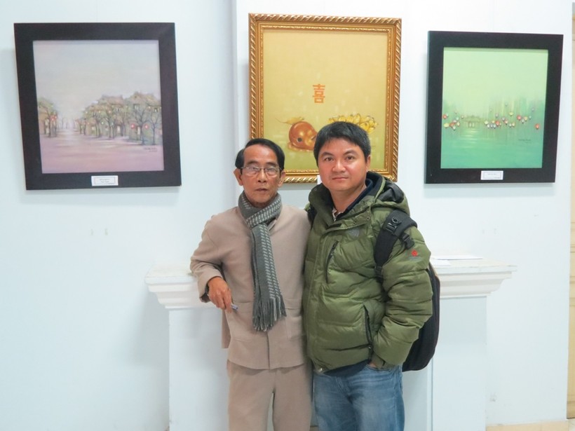Họa sĩ Thân Văn Huy (người đeo kính) chụp hình lưu niệm tại phòng triển lãm của mình 