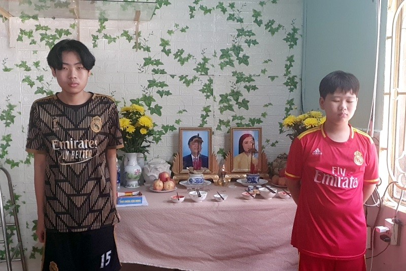 Hai anh em Phan Tuấn Kiệt và Phan Gia Lạc đứng trước di ảnh ba mẹ. 