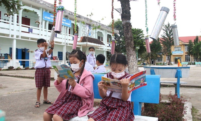 Các em đọc sách ở tủ sách di động dưới tán cây trong sân trường.