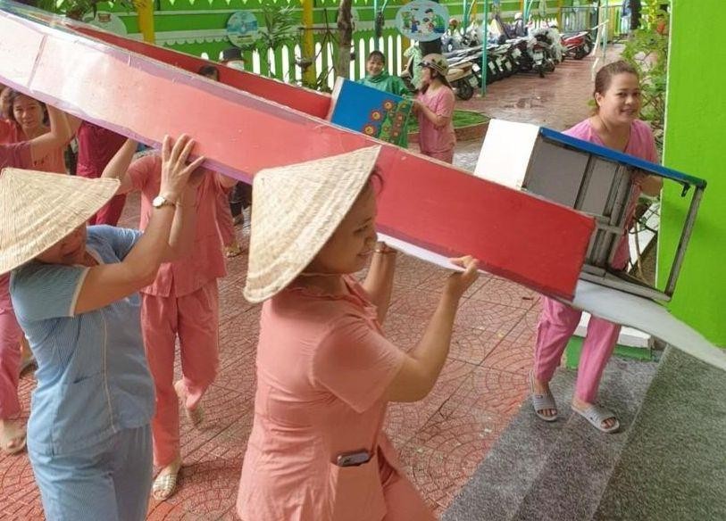 Giáo viên tại quận Liên Chiểu, huyện Hòa Vang di chuyển các thiết bị, đồ dùng ngoài trời vào khu vực an toàn trước khi bão đến. 