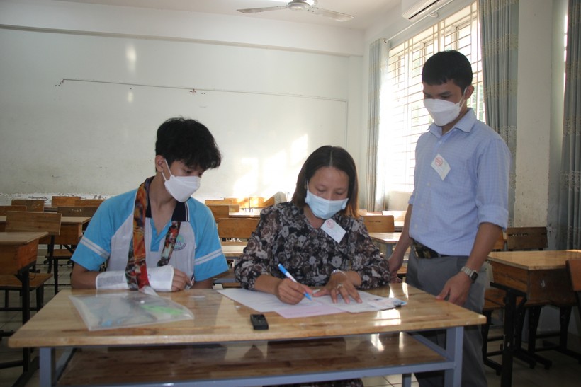 Học sinh không may bị gãy tay tại điểm thi Trường THCS Phạm Hữu Lầu được cán bộ coi thi hỗ trợ viết bài.