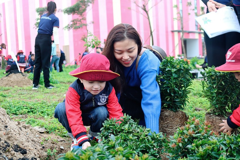 Một em học sinh mầm non tham  gia trồng cây cùng cô giáo