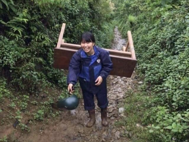 Cô Phan Thị Lục cõng trên vai chiếc bàn học vượt đèo dốc trơn trượt của rừng núi để đem tới điểm trường chính cho học sinh vào năm 2017. Ảnh: NVCC.