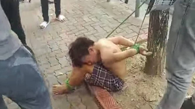 Thiếu niên bị trói cả 2 chân 2 tay tại gốc cây gần Công viên Thống Nhất, Hà Nội. Ảnh cắt từ clip.
