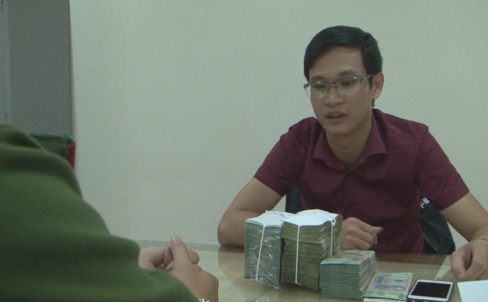 Đối tượng Phạm Văn Tới cùng số tiền bị thu giữ tại cơ quan điều tra, ảnh: QTV

